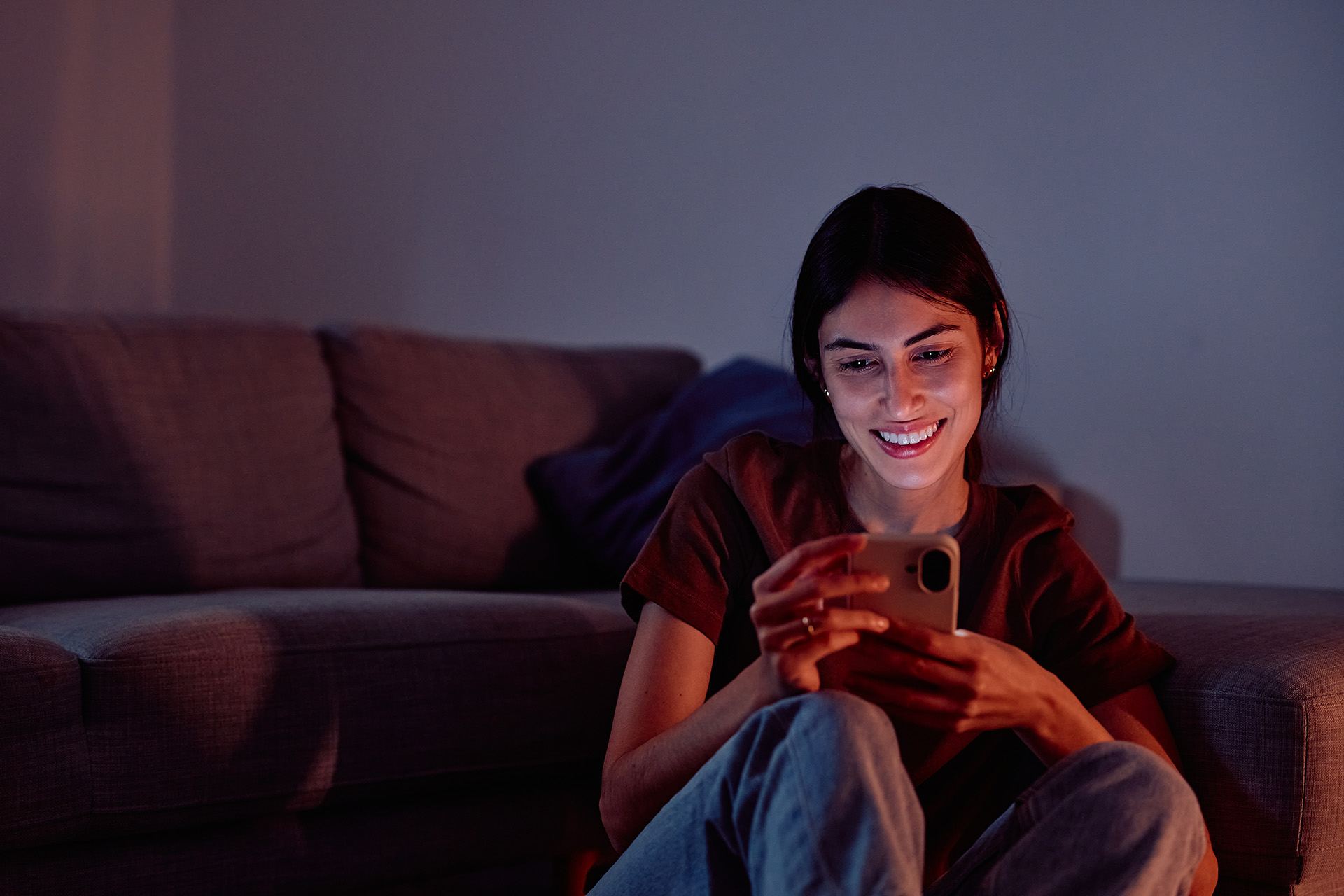 Persona usando su celular, sentada delante de un sillón.